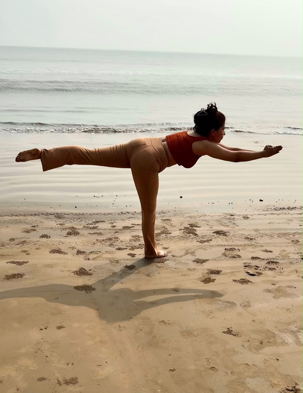 Woman in warrior III yoga pose on the beach